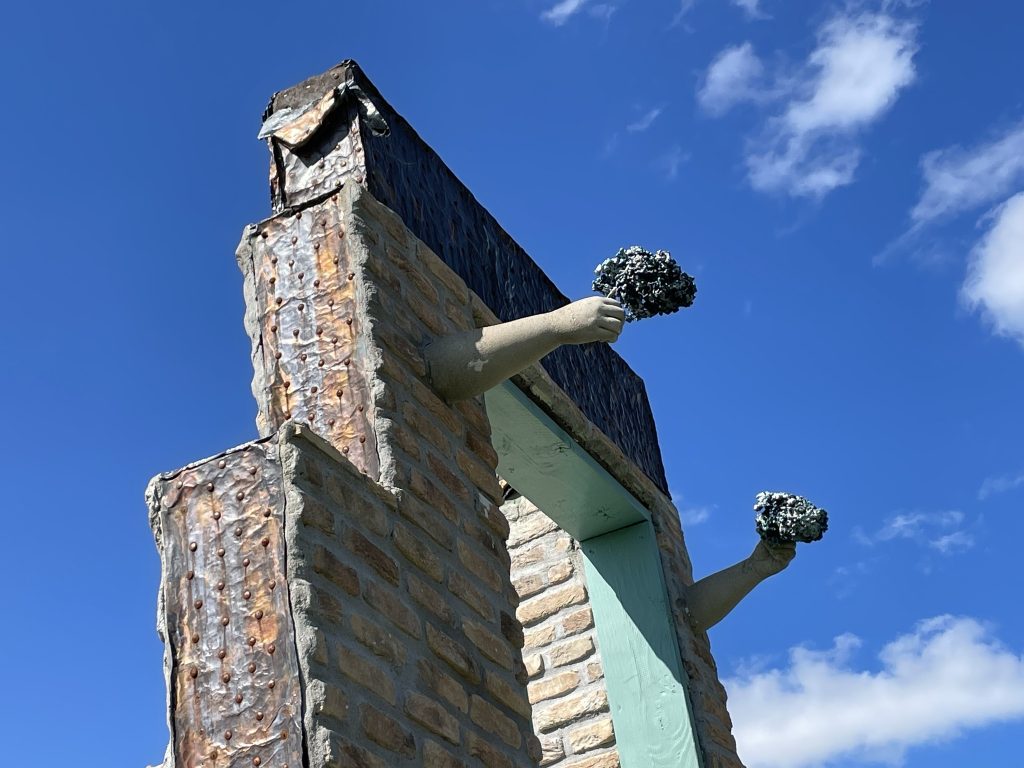 Stone sculpture of two figures with raised arms holding out flowers bright blue sky, symbolizing beauty in perseverance and achievement